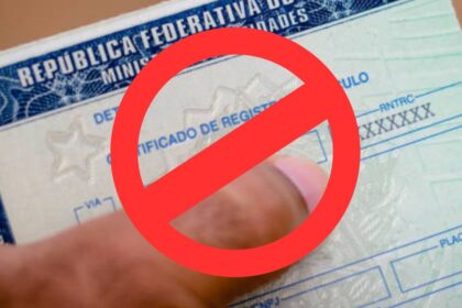 Pessoa segurando uma CNH com ícone de alerta em círculo vermelho, representando cassação da carteira de motorista.