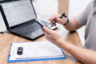 Pessoa consultando a situação documental veicular no celular, com notebook à direita.