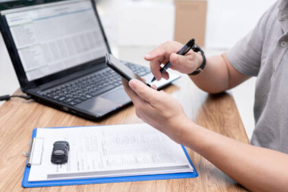 Pessoa consultando a situação documental veicular no celular, com notebook à direita.
