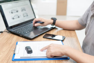 Pessoa digitando no notebook dados de um documento em papel A4, simbolizando atualização cadastral de veículo.