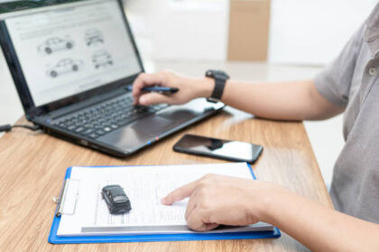 Pessoa digitando no notebook dados de um documento em papel A4, simbolizando atualização cadastral de veículo.