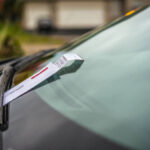 Veículo com um recibo de multa colocado no limpador de para-brisa.