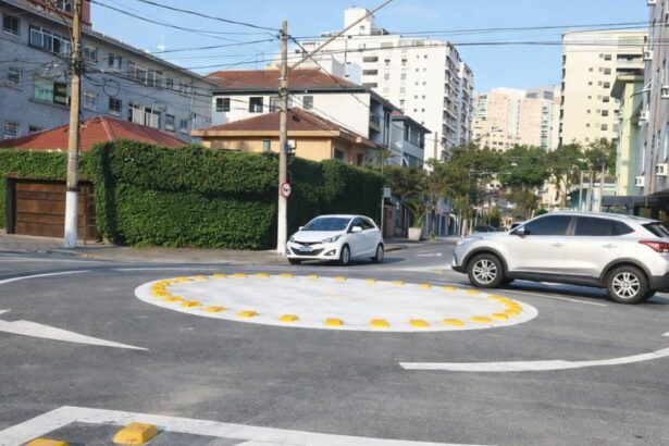 Mini rotatória urbana em cruzamento residencial com carros circulando e sinalização horizontal visível indicando sentido obrigatório